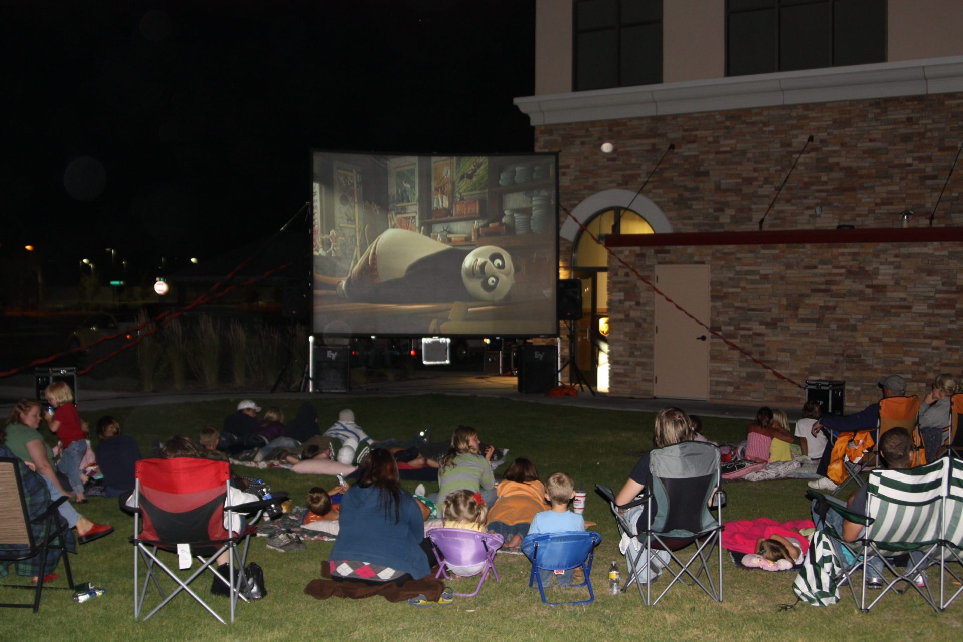 Families in lawn chairs watching an outdoor movie on an A&B Productions inflatable screen