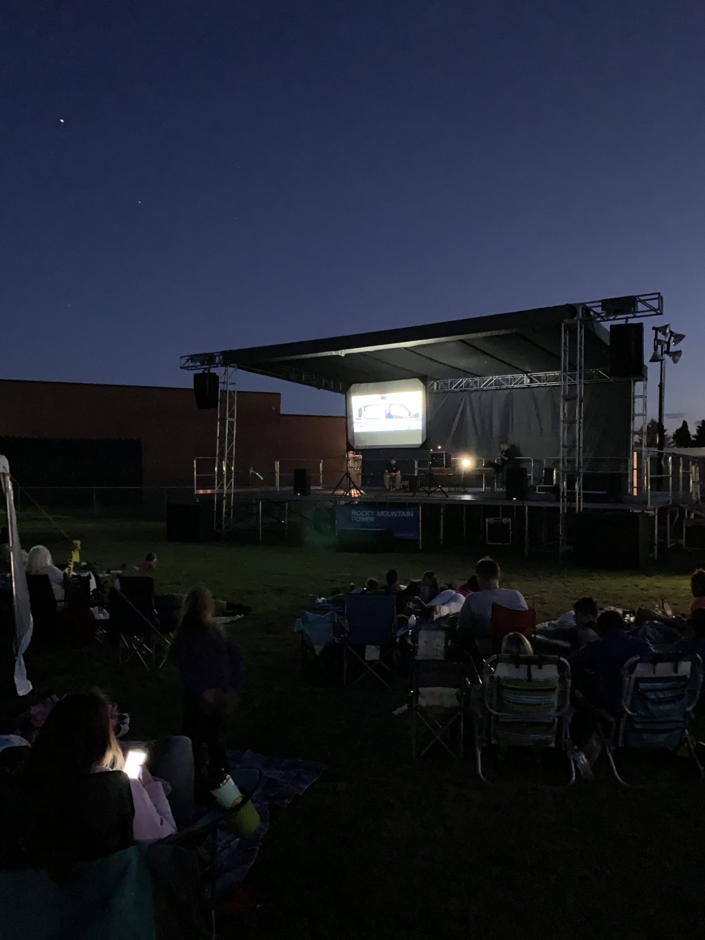 A&B Productions outdoor stage with a projection screen and sound system at dusk